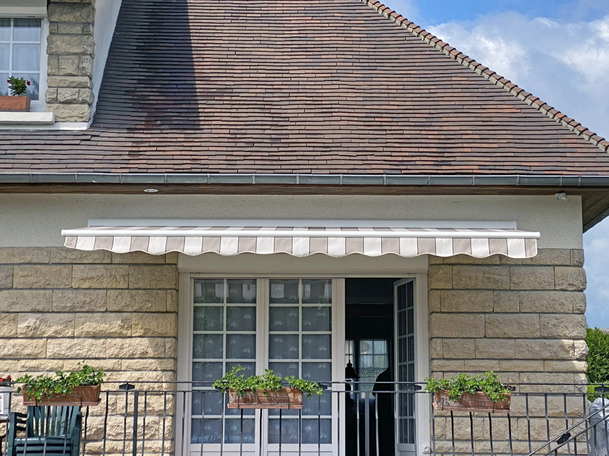 Façade d'une maison avec un auvent blanc et des pots de fleurs suspendus.
