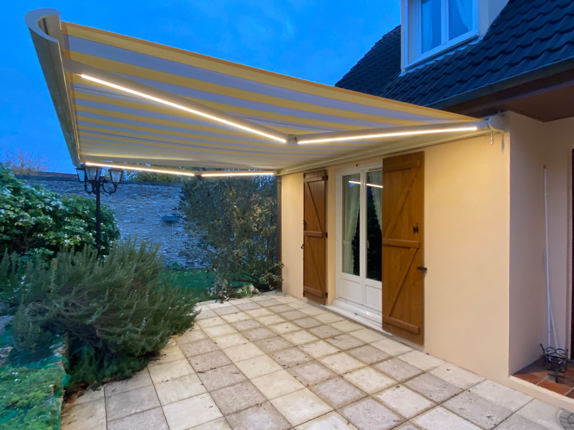 Auvent rétractable sur une terrasse, avec éclairage, devant une maison.