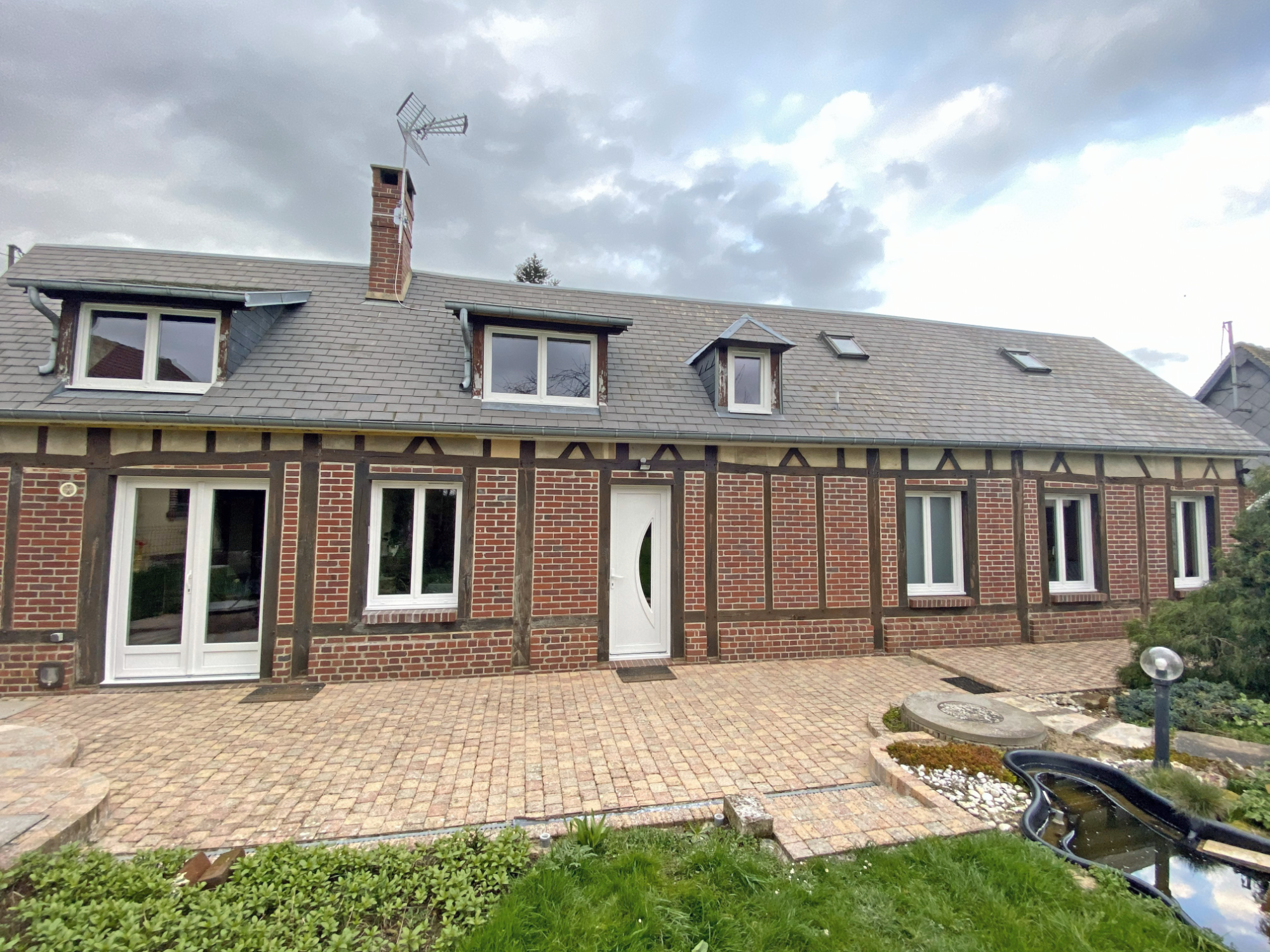 Maison en briques avec fenêtres blanches, toit en pente et jardin en parterre.