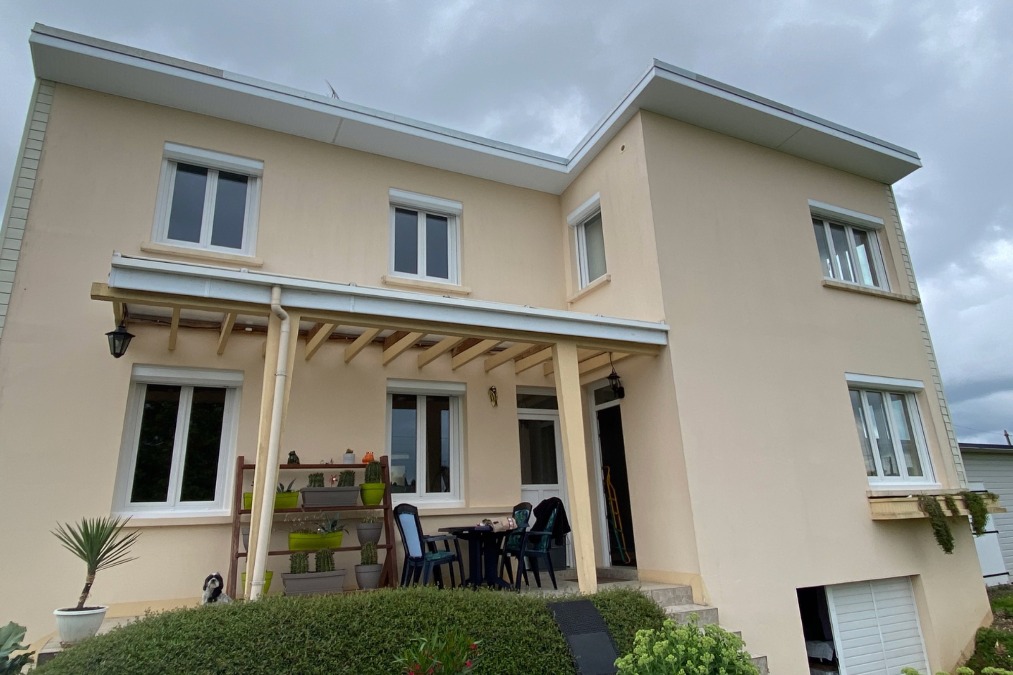 Maison à deux niveaux avec un porche et un petit jardin. Ciel nuageux en arrière-plan.