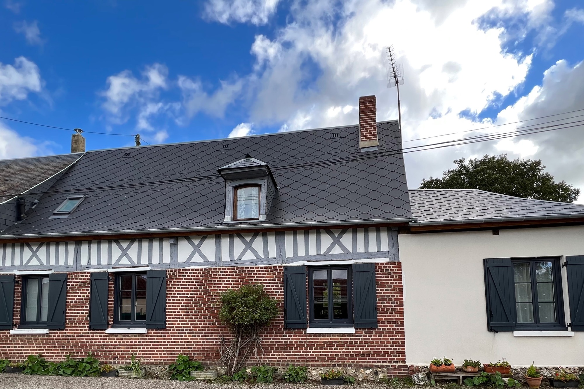 Maison de style normand avec toit en ardoise et murs en briques, sous un ciel nuageux.