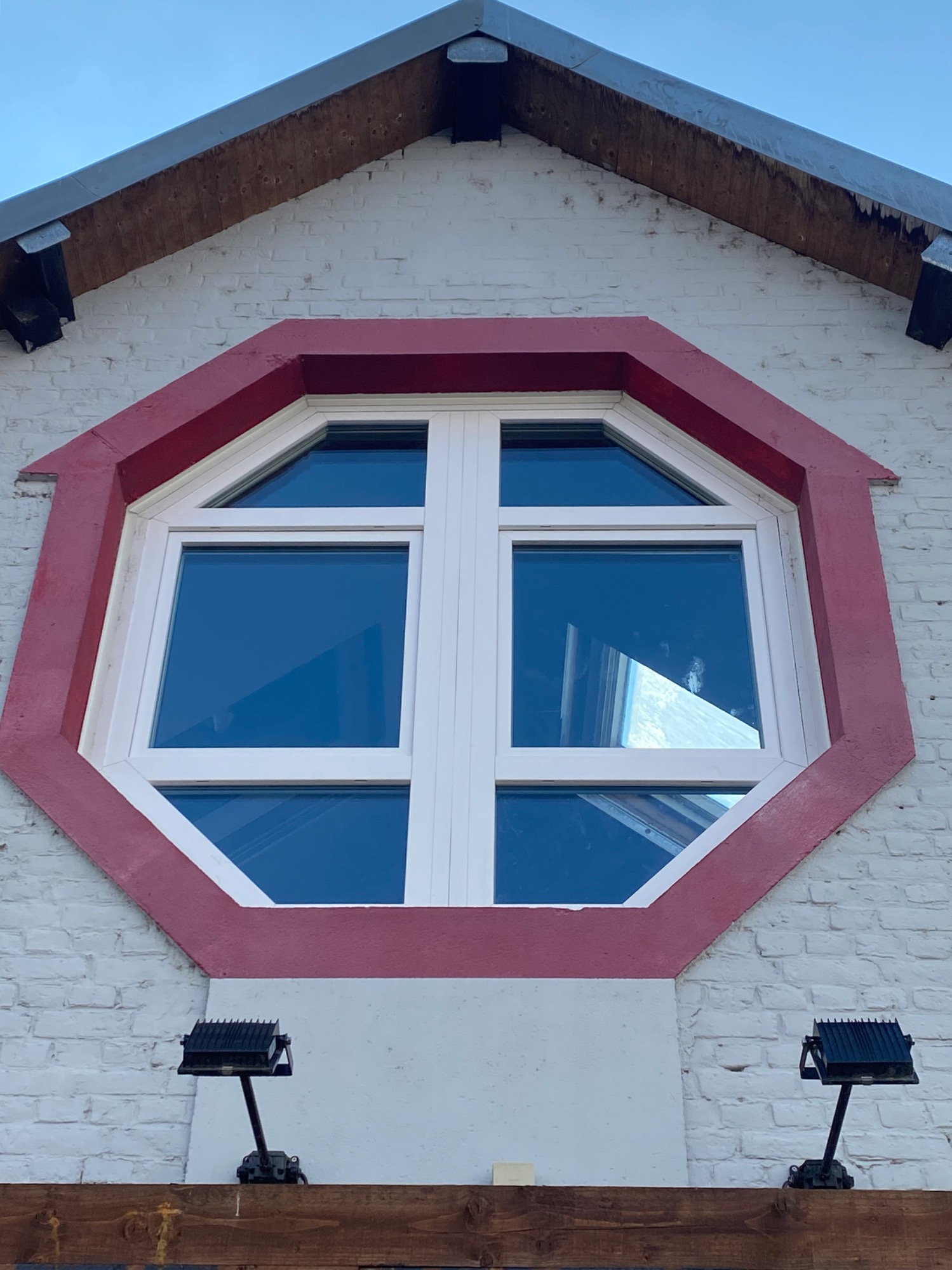Fenêtre octogonale avec encadrement rouge, située sous un toit en bois.