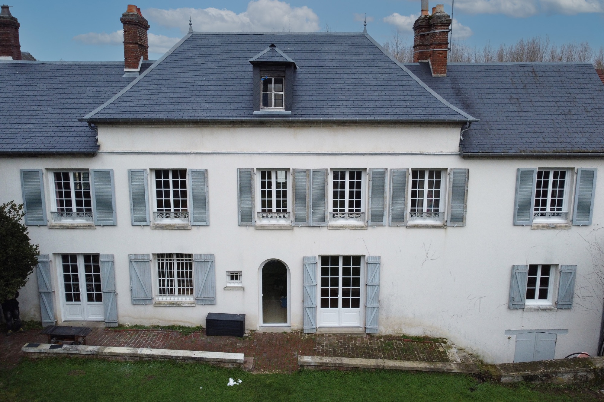 Maison blanche à deux étages avec des volets bleus et un jardin bien entretenu.