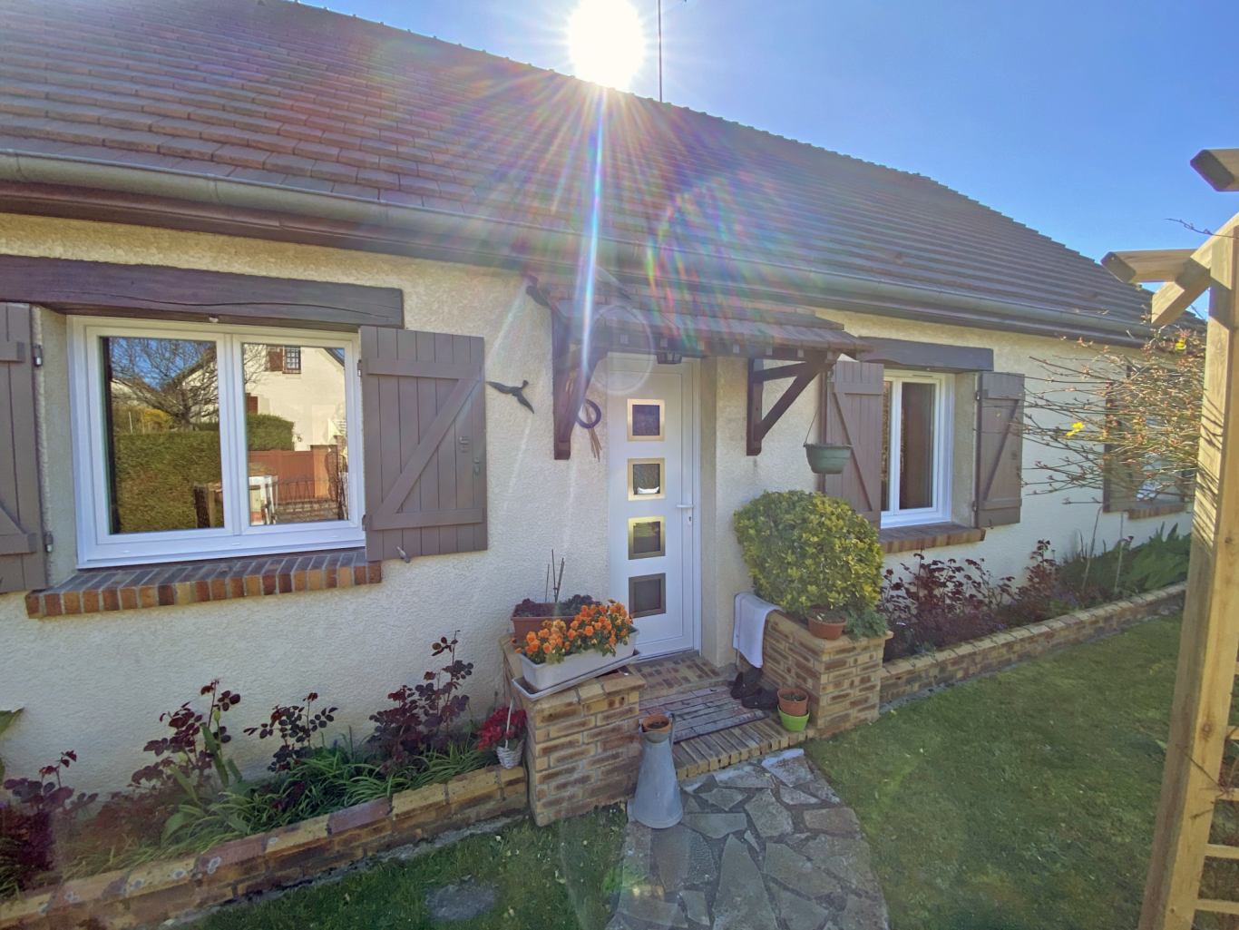 Maison avec fenêtres claires, volets, et petit jardin bien entretenu.