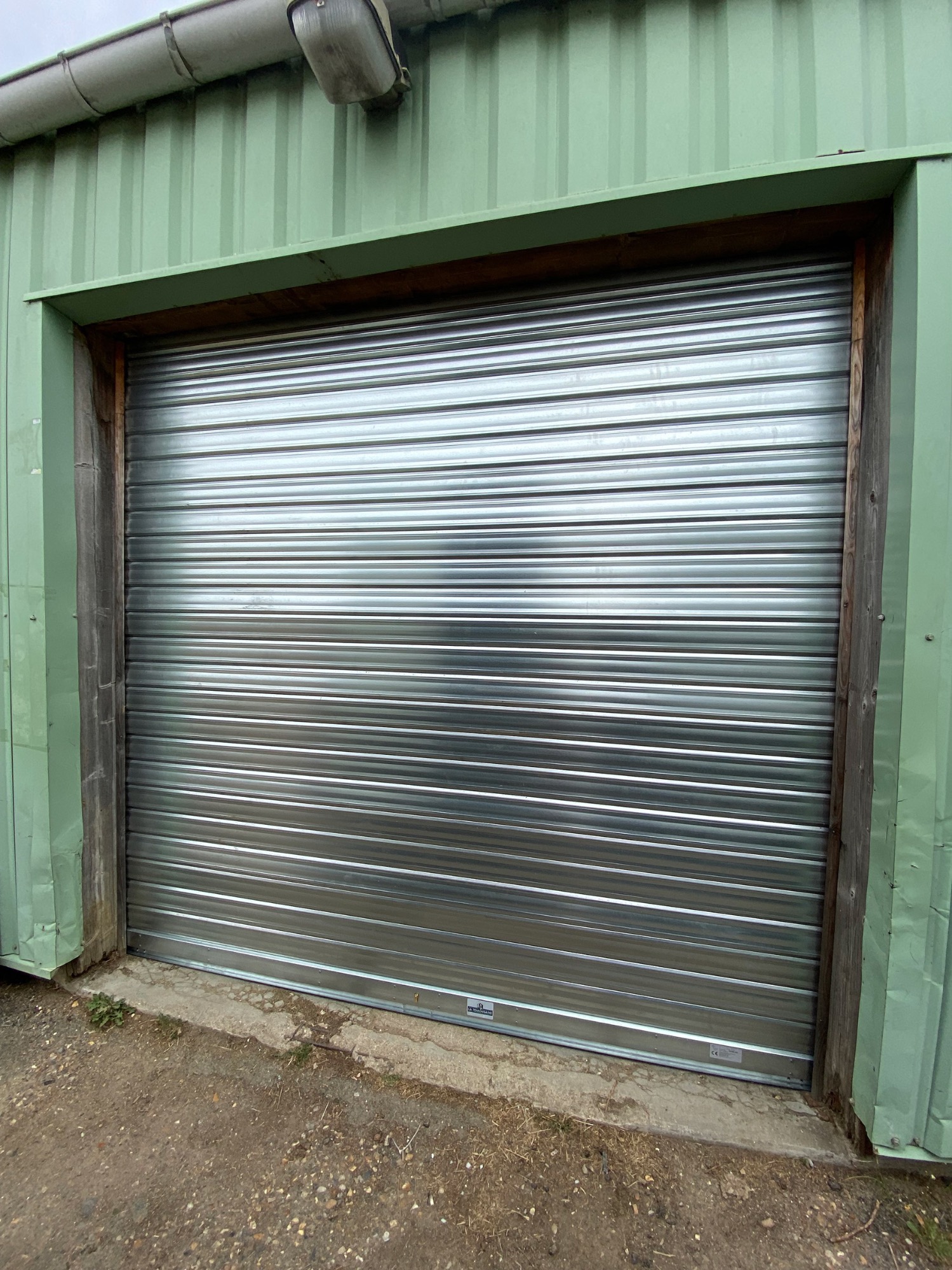 Porte de garage en métal roulant, avec une finition argentée et des panneaux horizontaux.