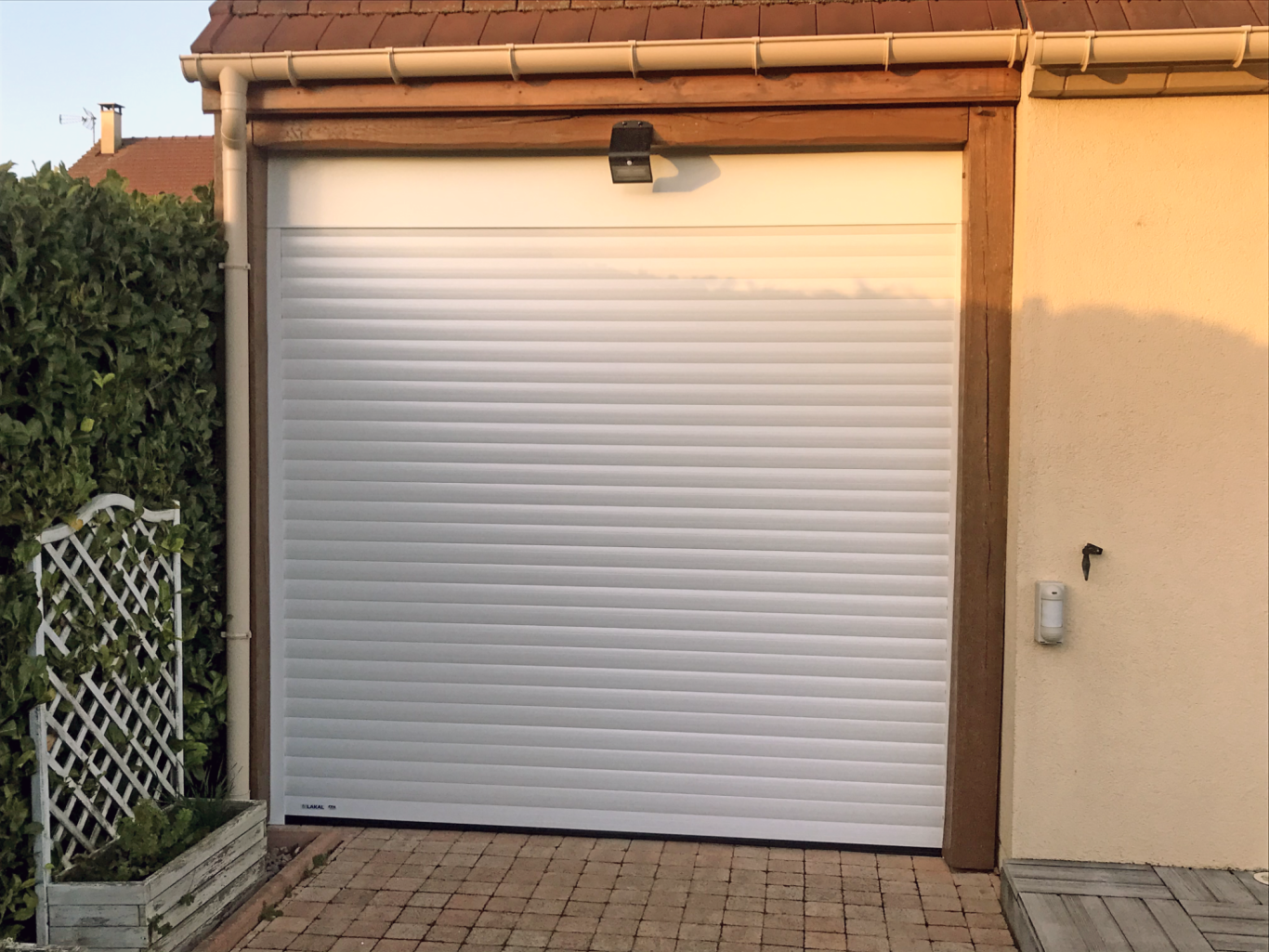 Porte de garage blanche enroulable, mur beige, avec un éclairage au-dessus.