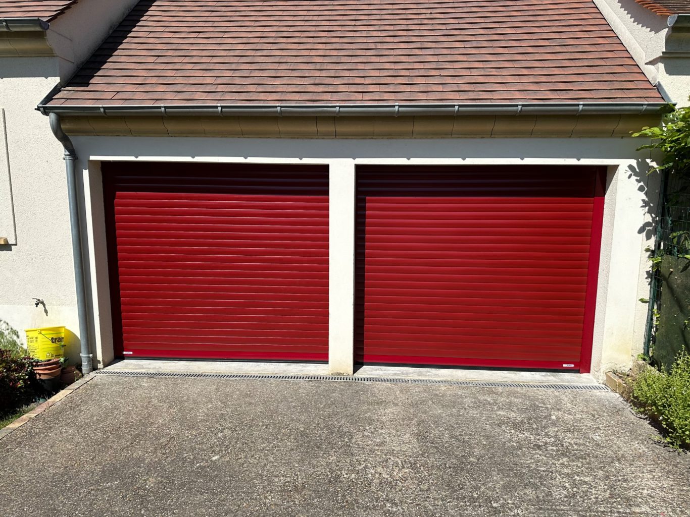 Deux portes de garage rouges sur un mur blanc, avec un toit en pente au-dessus.