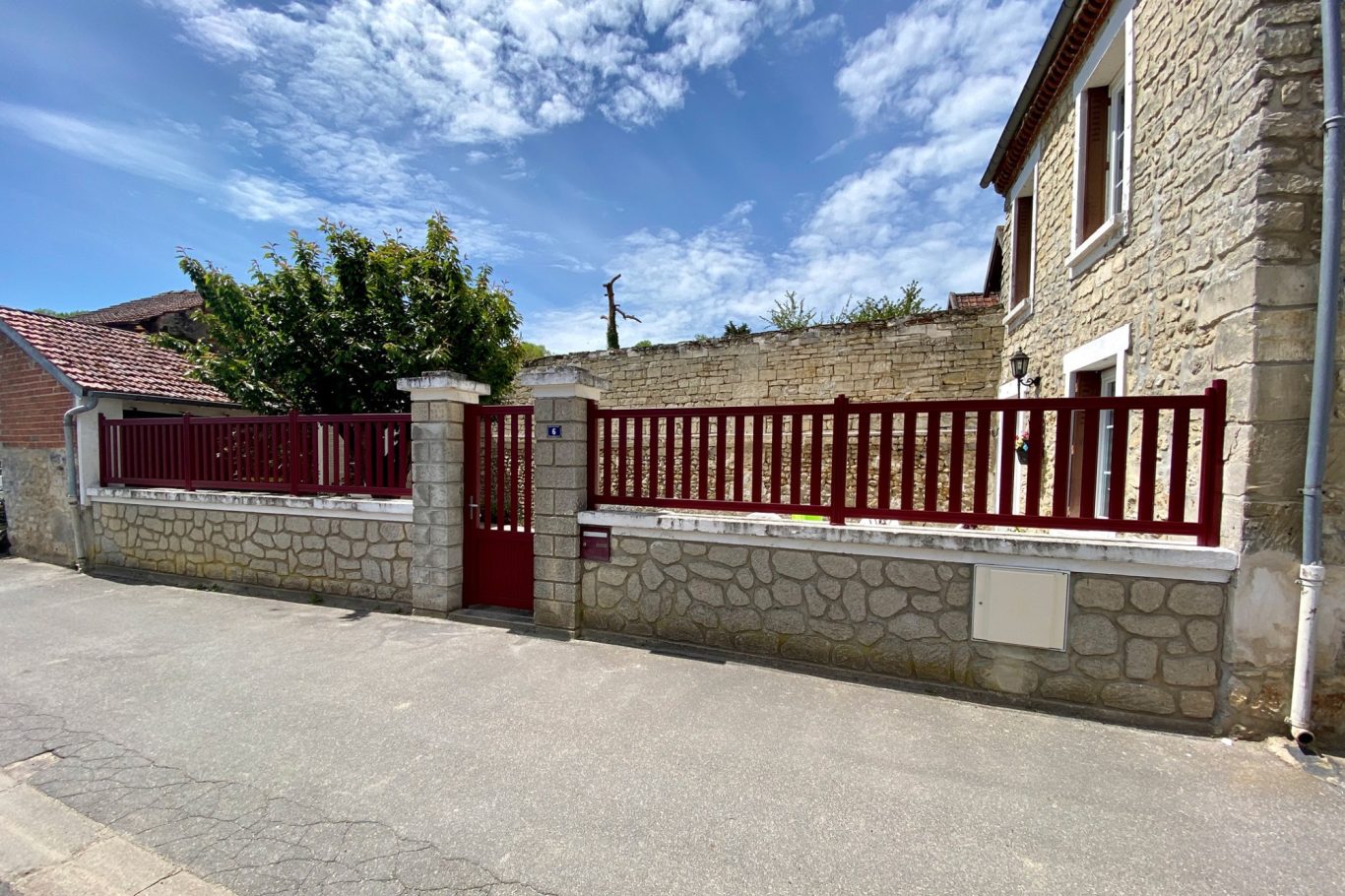 Mur en pierre avec clôture rouge et porte, sous un ciel partiellement nuageux.