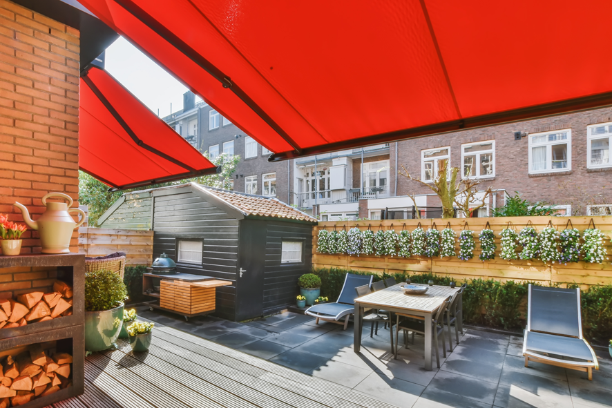 Pose de stores bannes à hébécourt | DJS Fermetures Terrasse ensoleillée avec parasols rouges, table, chaises et murs végétalisés.