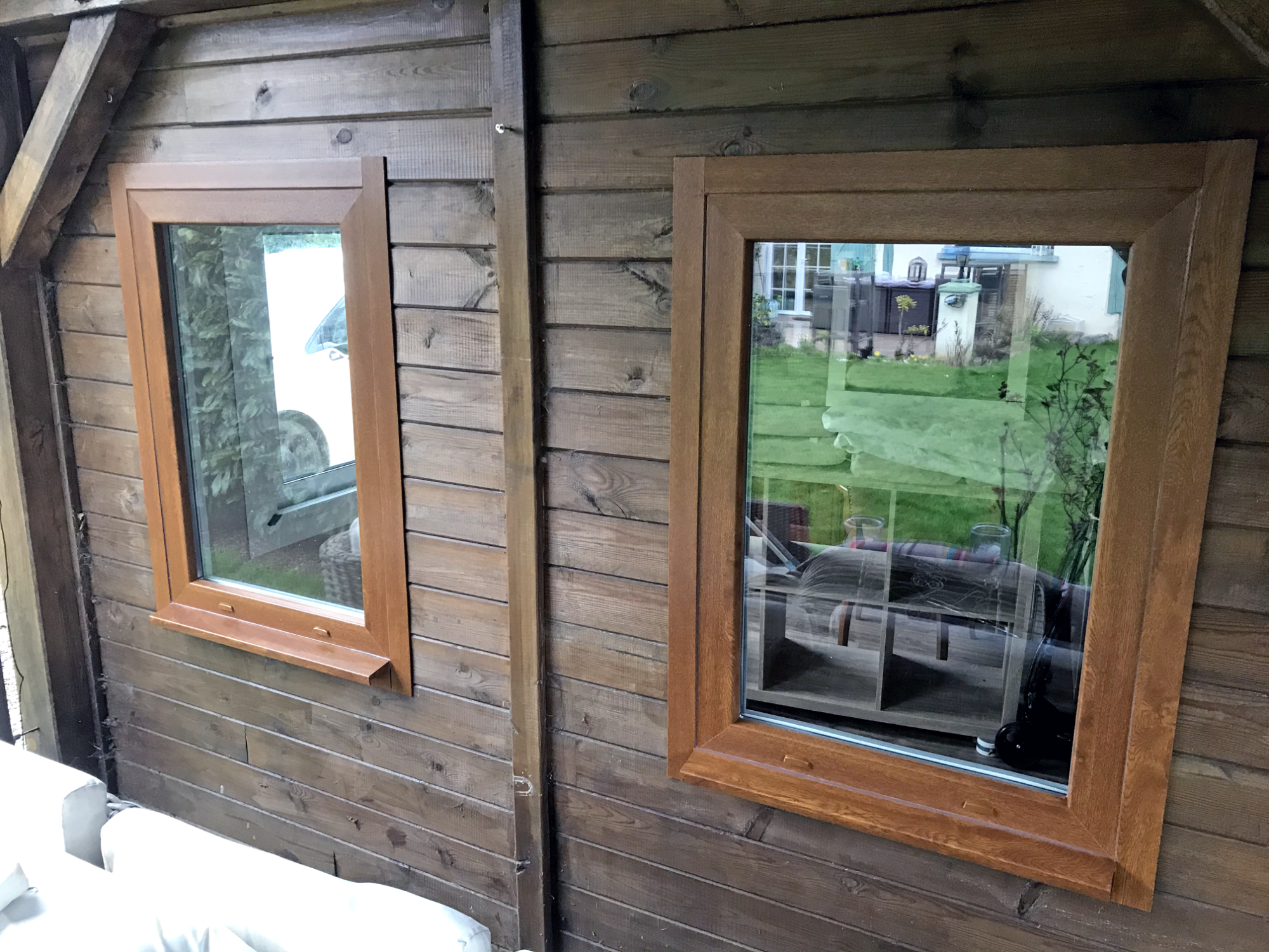 Deux fenêtres en bois sur un mur en bois, avec vue sur un jardin.