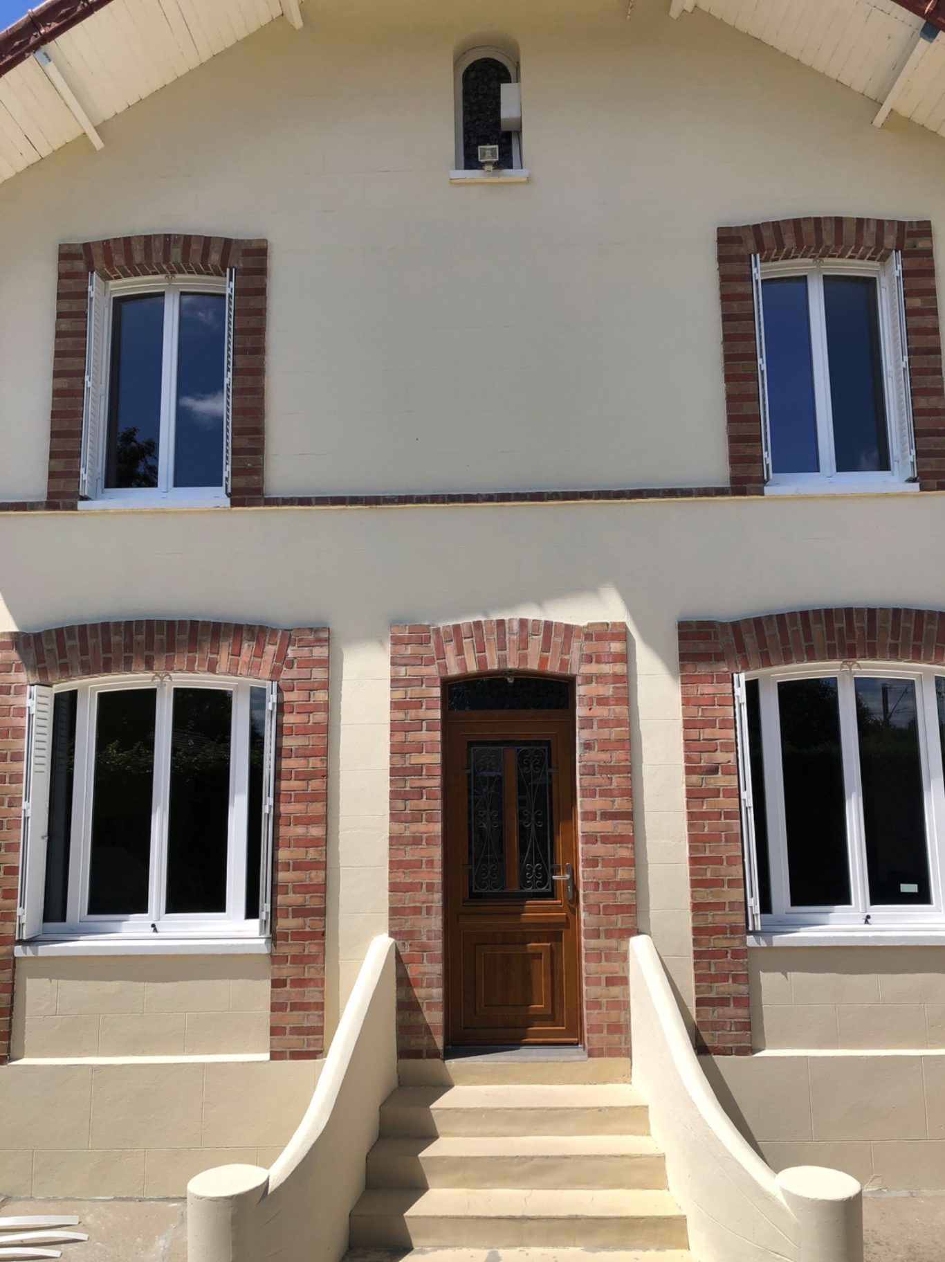 Façade d'une maison avec une porte en bois et des fenêtres à encadrement de brique.