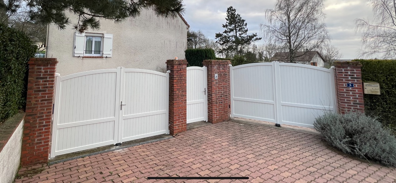 Portail blanc en briques, entrée d'une maison avec des buissons.