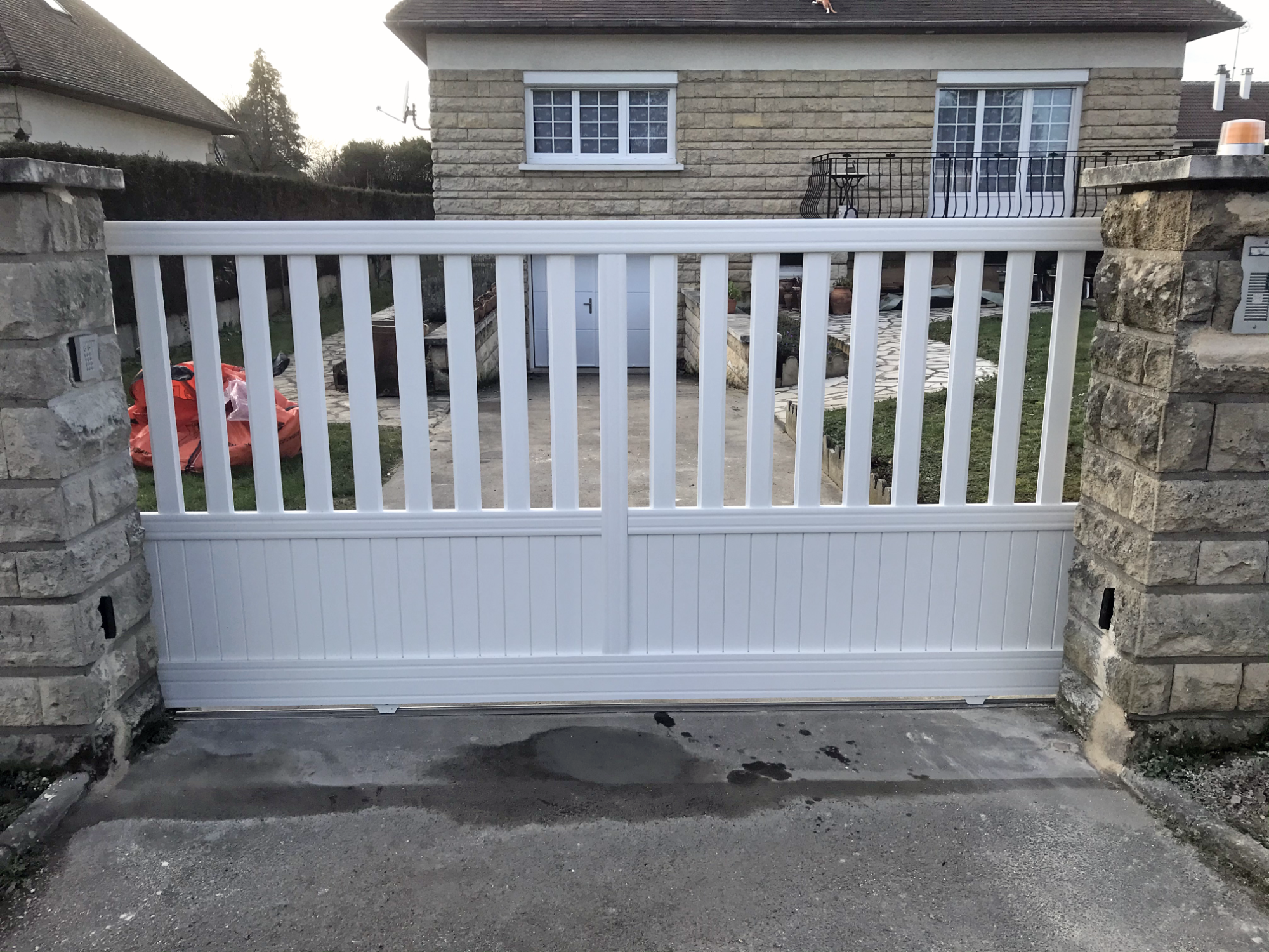 Portail en bois blanc avec des lattes, devant une maison en pierre.