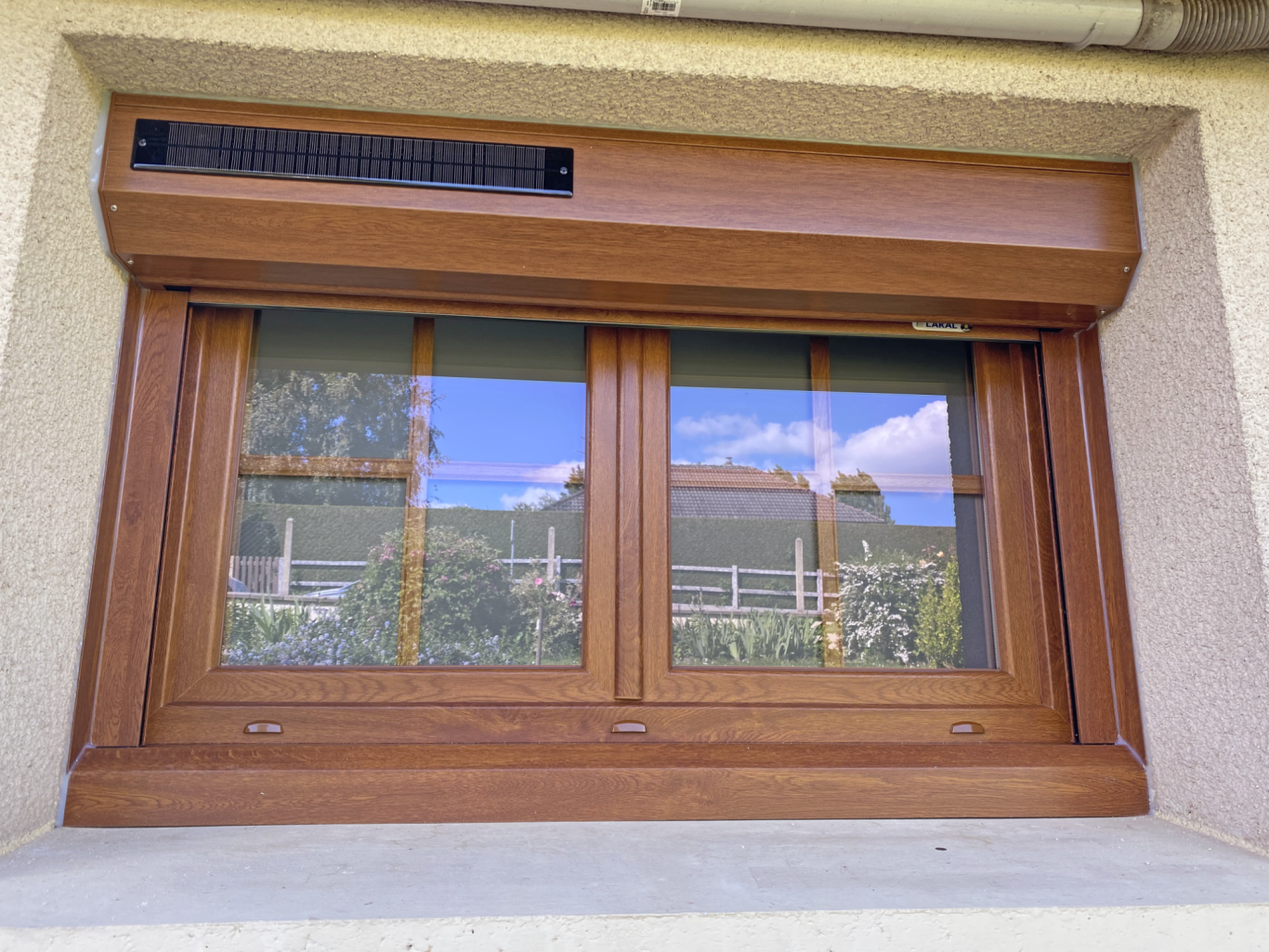 Fenêtre en bois avec volets, vue sur un jardin et ciel bleu.